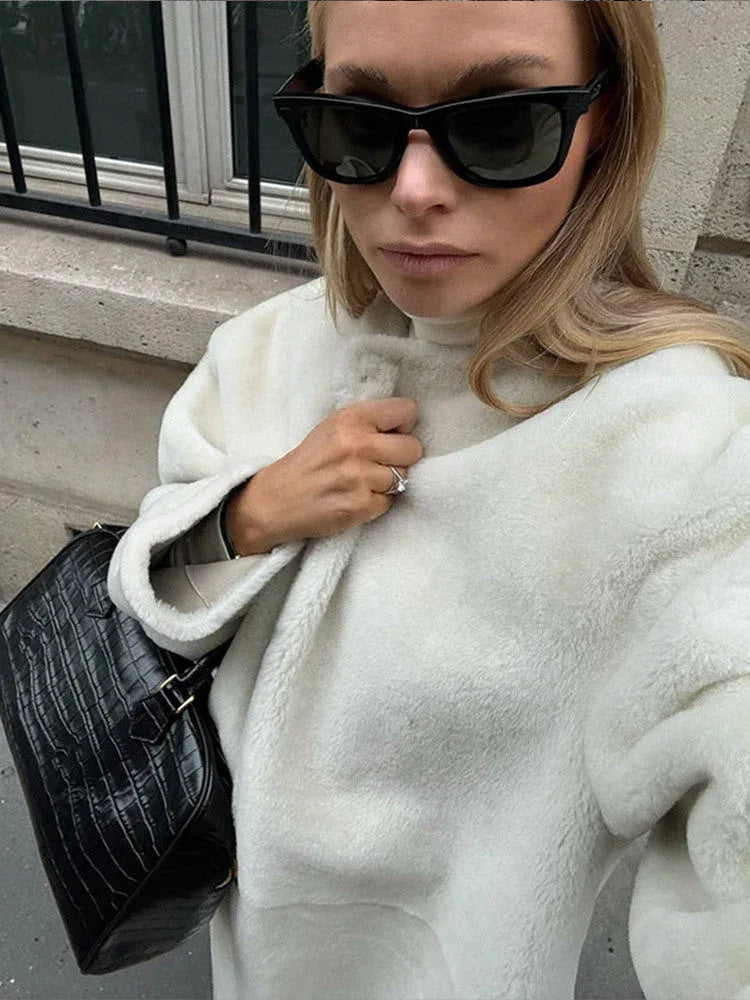 Close-up of a woman wearing a cream-colored sherpa fleece coat and black sunglasses.