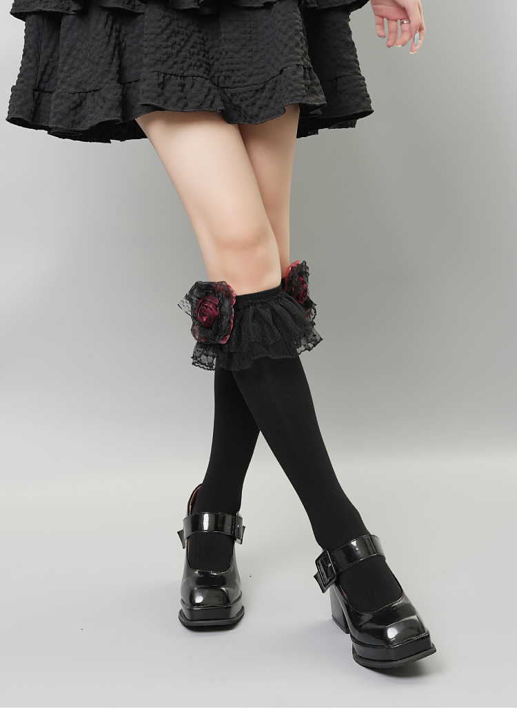 Model wearing black knee-high socks with lace and rose details, paired with platform shoes.