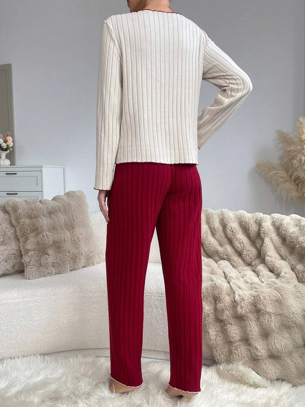 Back view of a woman in a cream ribbed knit top and red ribbed knit pants.