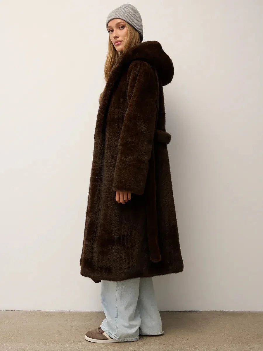 Side view of a woman in a long brown faux fur coat with a hood and light wash jeans.