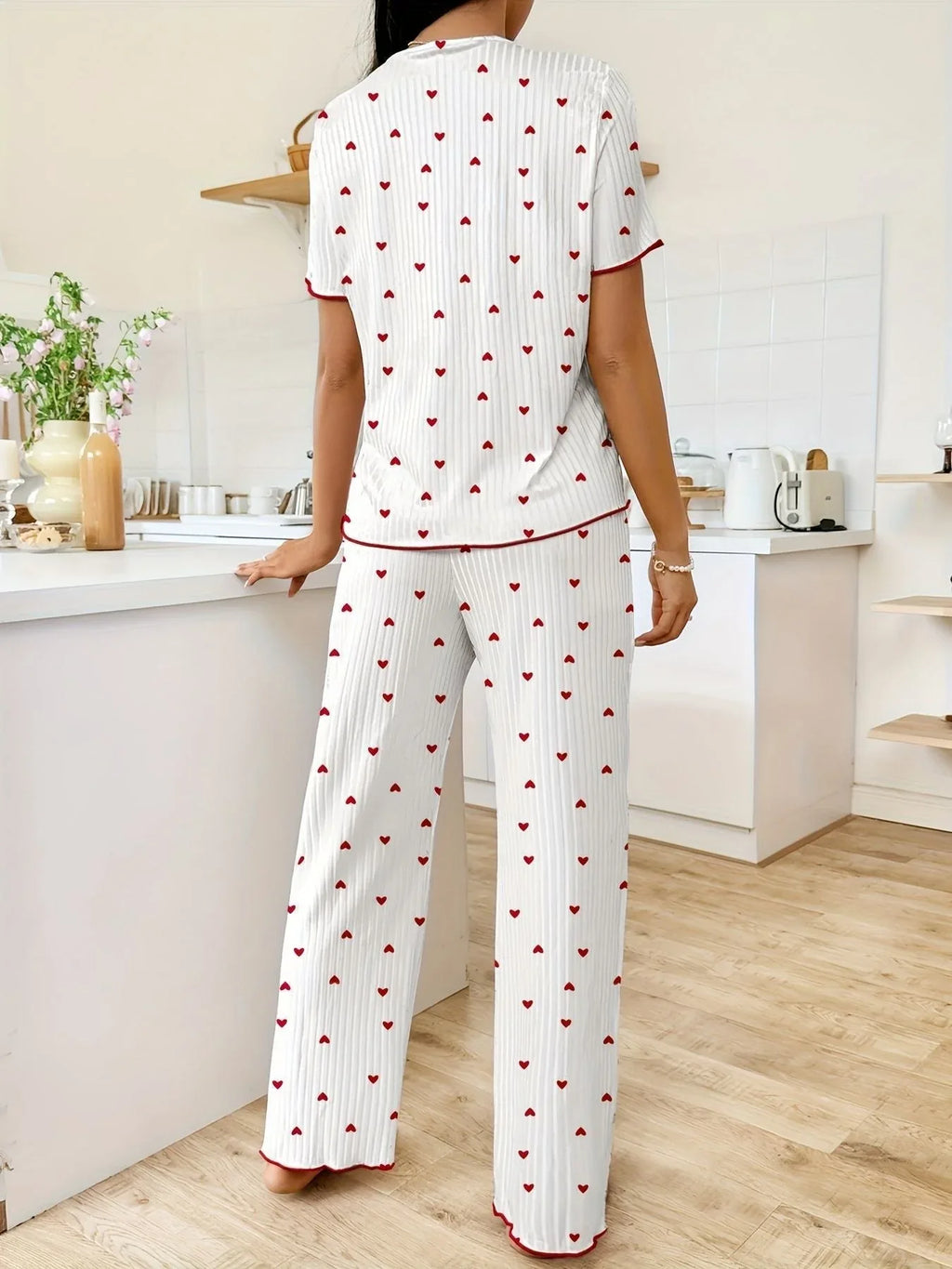 Back view of a woman wearing white pajama set with red hearts and red trim, standing in a kitchen.
