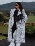 Woman in a long white and black spotted faux fur coat and black outfit outdoors.