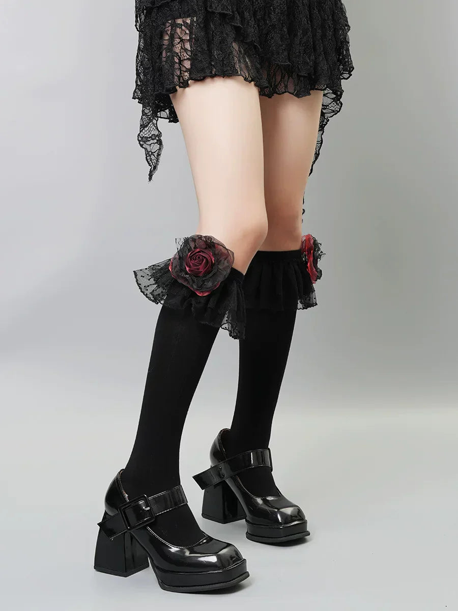 Black knee-high socks with ruffled lace trim and red rose embellishments on the calf.