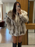 Full body shot of a woman wearing a luxurious faux fur jacket over a white top and dark boots.