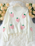 White cropped knit sweater with embroidered pink strawberry appliques and green stems, displayed on a hanger with a floral backdrop.
