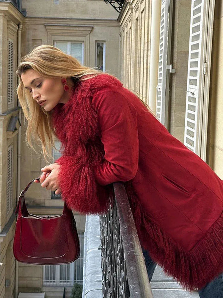 Woman leaning on a balcony railing, wearing a red suede coat with faux fur trim and cuffs.