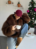 Woman wearing a brown faux fur jacket and blue jeans drinking coffee indoors