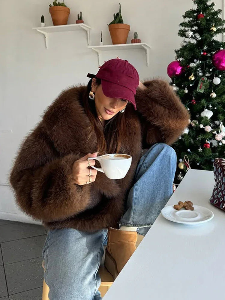 Woman wearing a brown faux fur jacket and blue jeans drinking coffee indoors