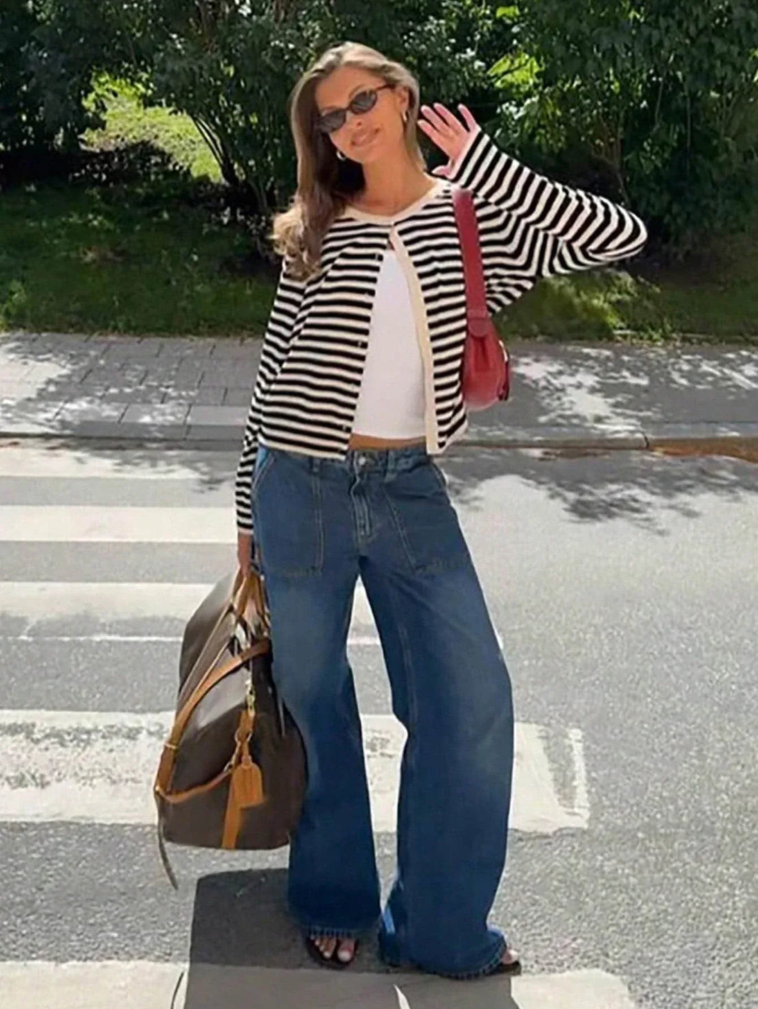 Woman wearing a black and white striped cardigan with a white tank top and blue wide-leg jeans standing on a crosswalk.
