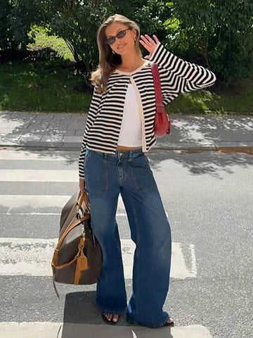 Woman wearing a black and white striped cardigan with a white tank top and blue wide-leg jeans standing on a crosswalk.