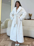 Woman wearing a white faux fur longline coat with chevron texture and a belted waist, standing indoors in a living room.