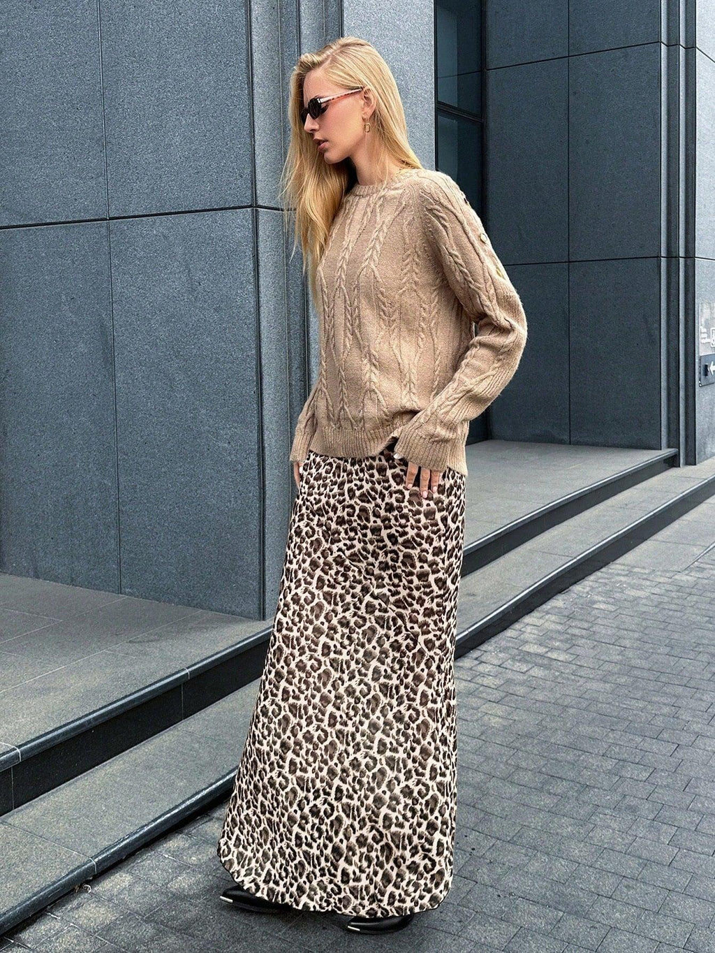 Woman with a white purse slung over her shoulder, wearing a tan textured knit sweater and blue jeans.