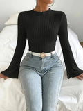 Front view of a woman in a black ribbed knit top with flared sleeves and a mock neck, styled with blue denim jeans and a white belt.