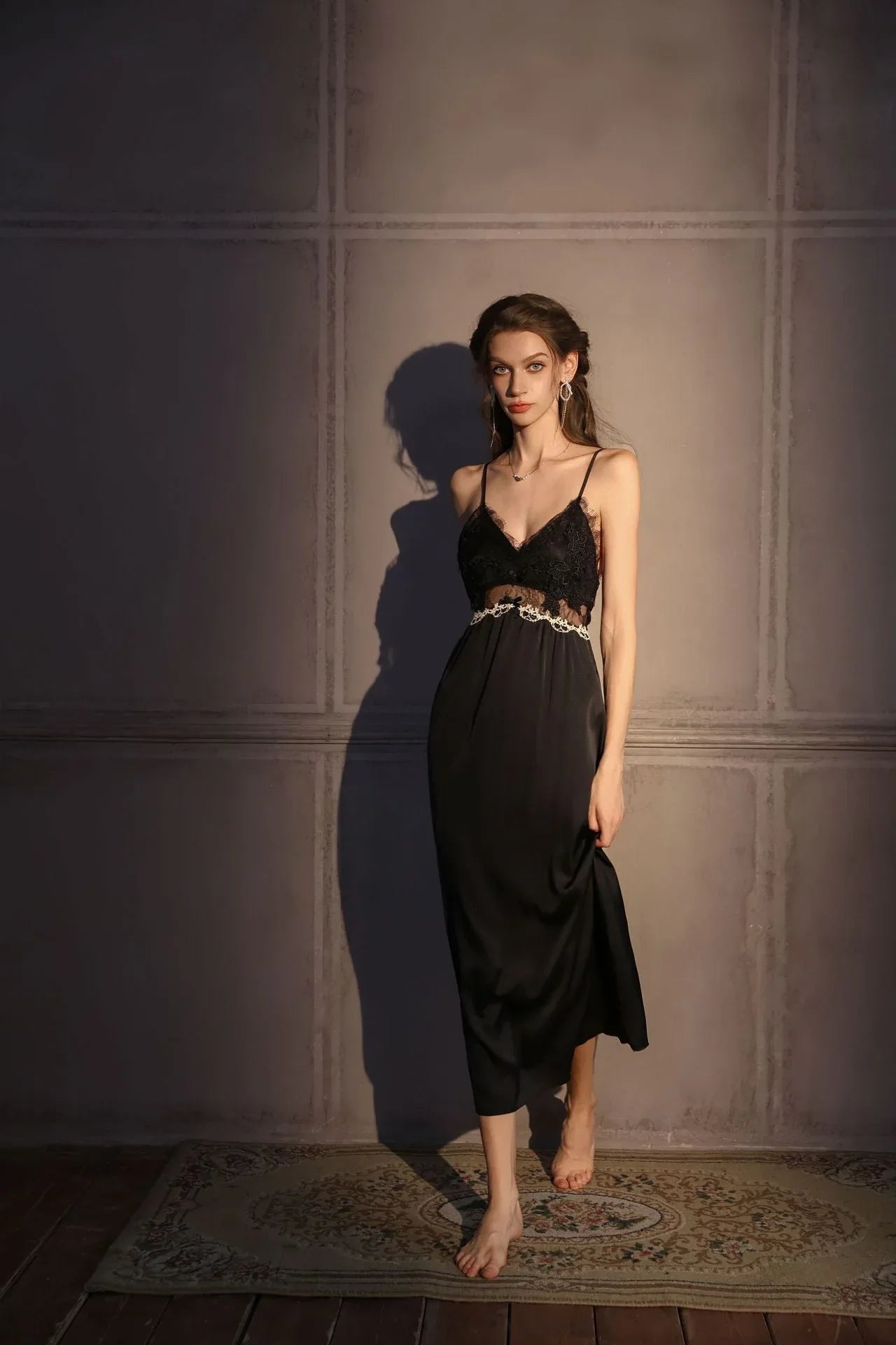 Woman in a black satin slip dress with lace bust detail, lifting the hem of the dress.