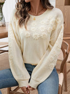 Woman seated, showcasing a cream knit sweater with floral embellishments and balloon sleeves.