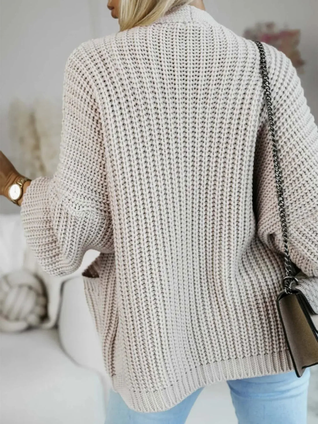 Woman wearing a beige chunky knit cardigan with open front and patch pockets.