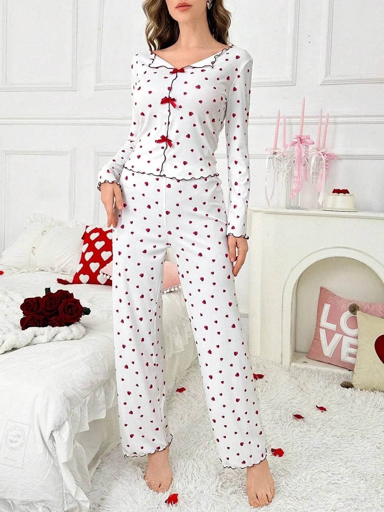 Woman wearing a white long-sleeve pajama set with a red heart print and red trim, standing in a room with red heart balloons.