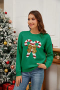 Woman wearing a green knit sweater with a candy cane sequin design, smiling and holding a gift.