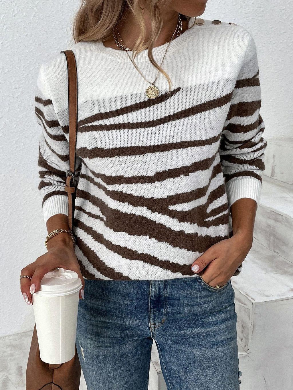 Woman wearing a white and brown zebra print crew neck sweater with gold shoulder buttons