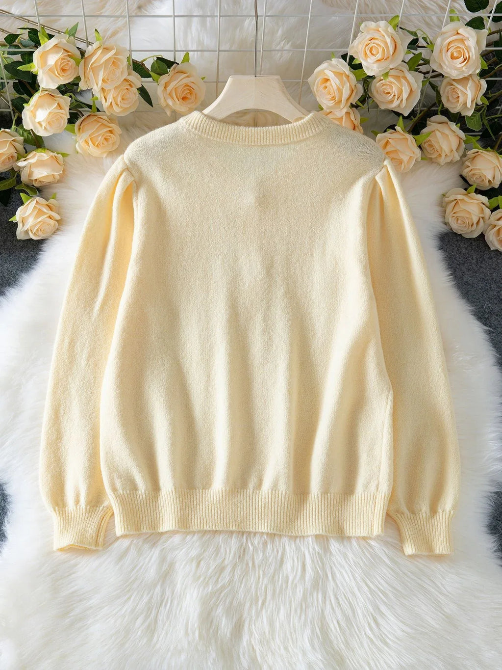 Back view of light yellow knit cardigan with puff sleeves laid flat