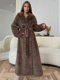 Woman wearing a long, brown faux fur coat with a chevron pattern and a belted waist, posing indoors.