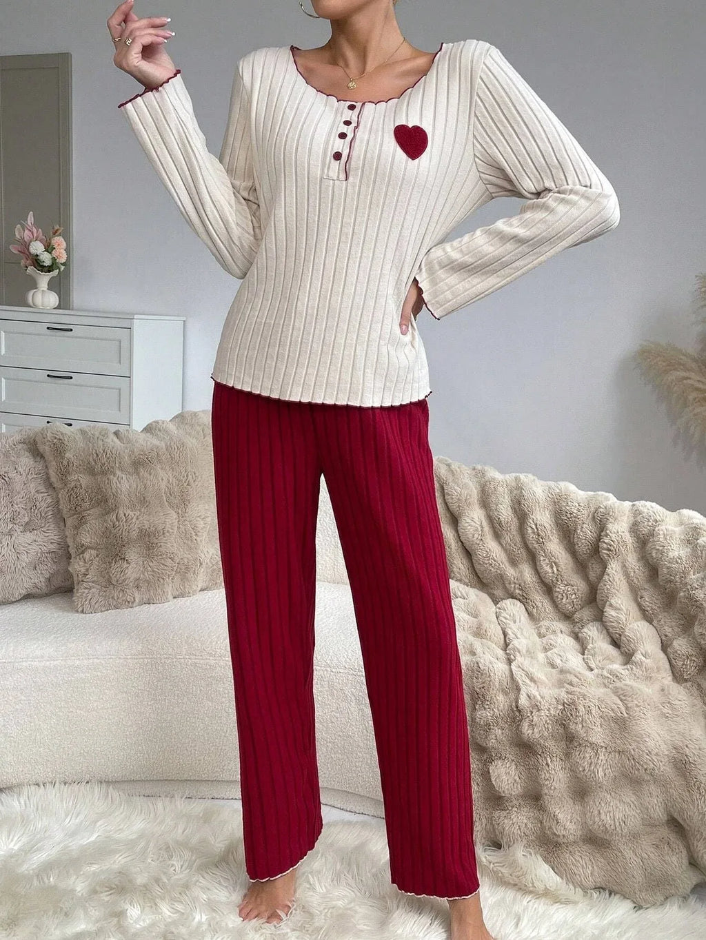 Woman wearing a cream ribbed long-sleeve top with a red heart applique and red ribbed wide-leg pants.