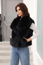 Woman wearing a black faux fur vest and blue jeans, with hands on hips, looking to the side.