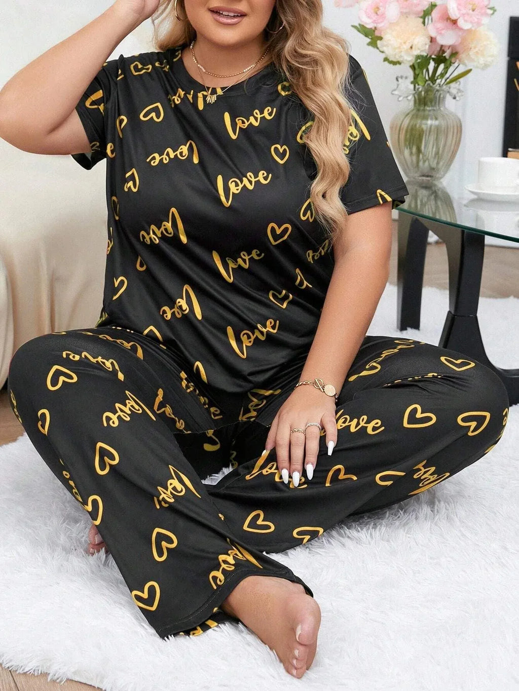 Woman wearing a black short-sleeve pajama top and pants with a gold heart and 'love' graphic print, sitting on the floor.