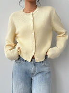 Woman posing in a light yellow knit cardigan and denim jeans.
