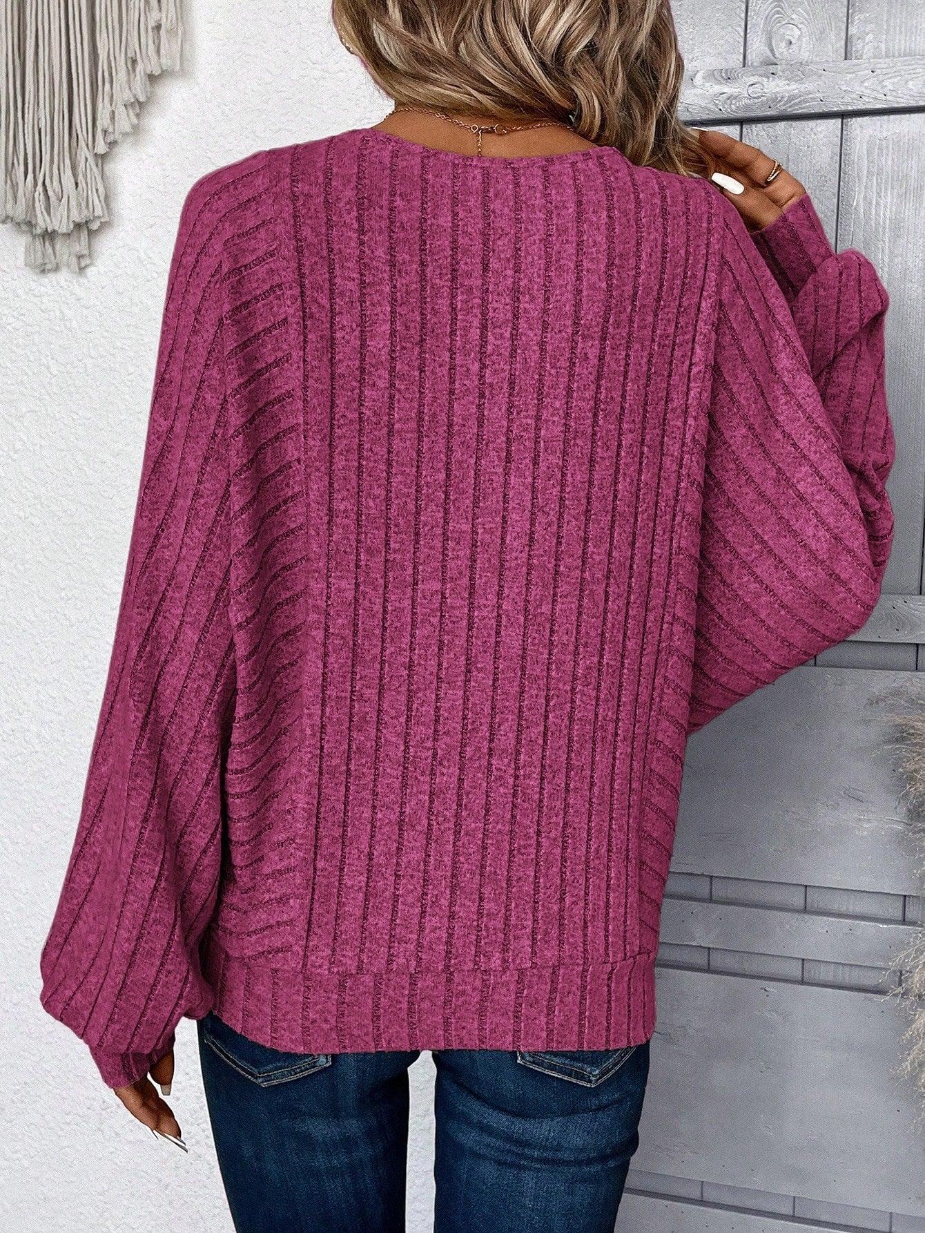Back view of a woman wearing a magenta ribbed knit sweater with wide sleeves.
