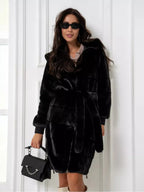 Woman wearing a black hooded faux fur coat with a belted waist and zipper closure.