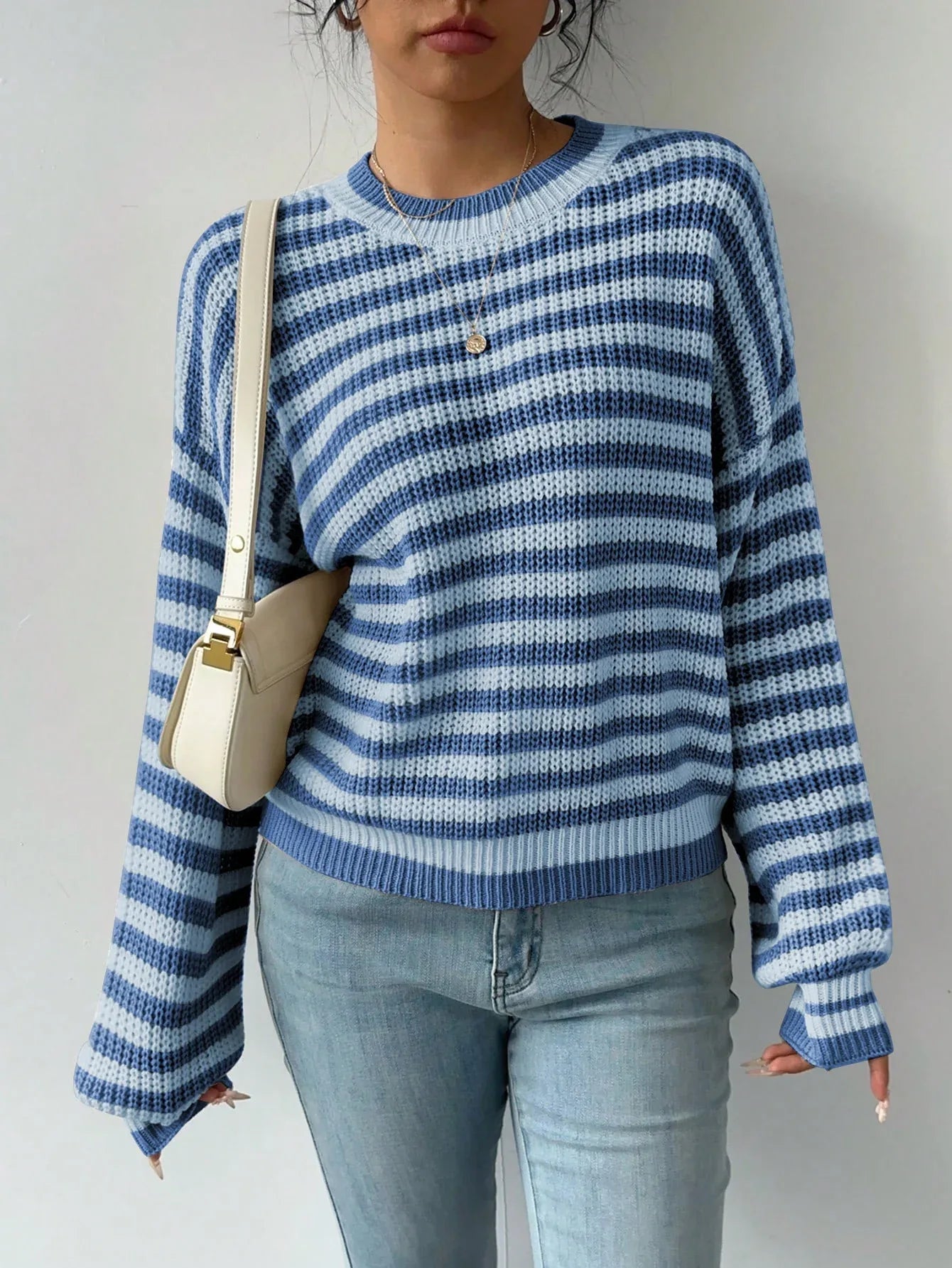 Woman wearing a blue and white striped knit sweater, paired with light wash denim jeans