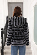 Rear view of a woman in a hooded, belted, grey and black striped faux fur jacket.