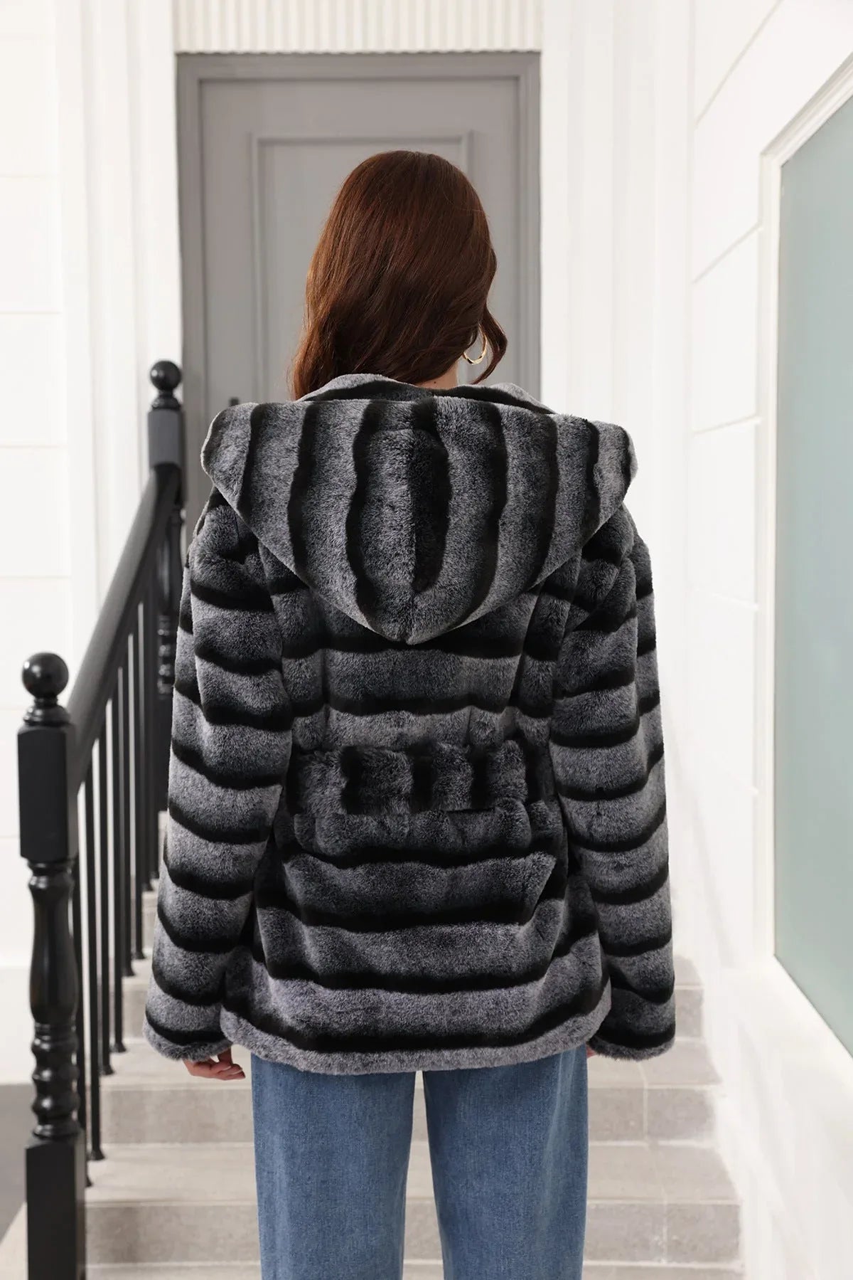 Rear view of a woman in a hooded, belted, grey and black striped faux fur jacket.