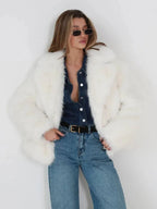 Woman styled in a white faux fur jacket, denim shirt, and jeans, with hands in pockets.