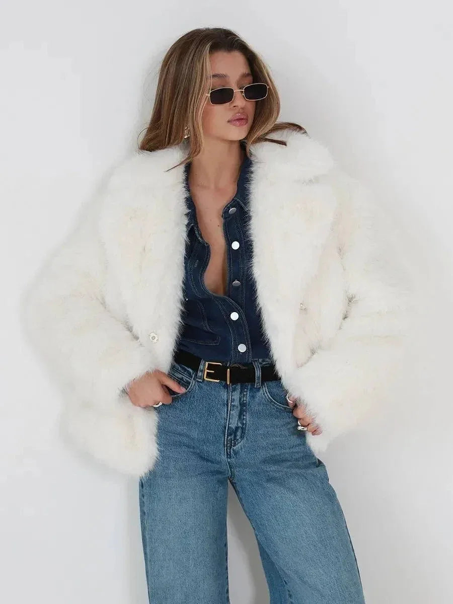 Woman styled in a white faux fur jacket, denim shirt, and jeans, with hands in pockets.