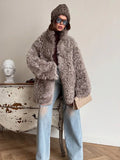 Woman wearing a grey curly faux fur oversized coat with a brown turtleneck and light blue ripped jeans, holding a cream clutch.