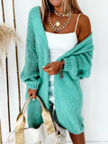 Woman wearing a longline teal chunky knit cardigan over a white tank top and denim shorts, holding a gold tote bag.