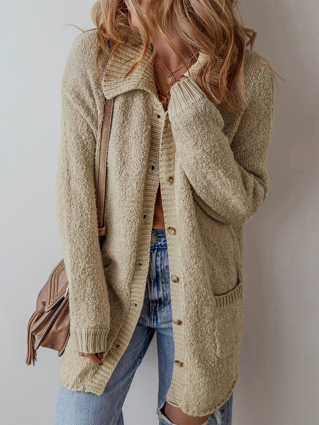 Woman wearing a longline beige textured knit cardigan with a pointed collar and button-up closure.