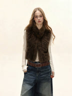 Woman wearing a brown faux fur vest over a white long-sleeve shirt and denim skirt.