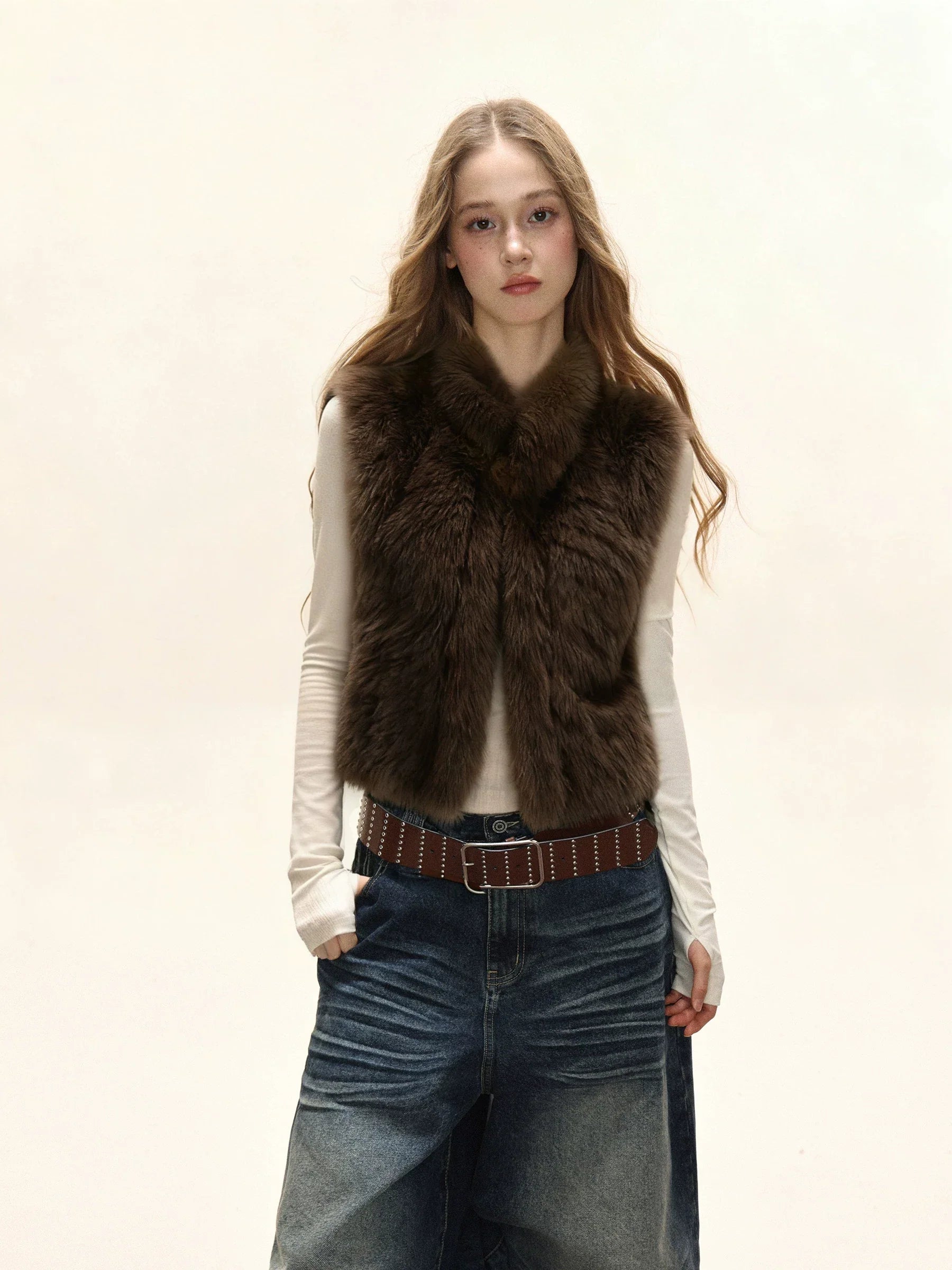 Woman wearing a brown faux fur vest over a white long-sleeve shirt and denim skirt.