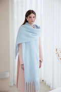 Full body shot of a woman wearing a light blue oversized scarf with fringe detail over a pink coat.