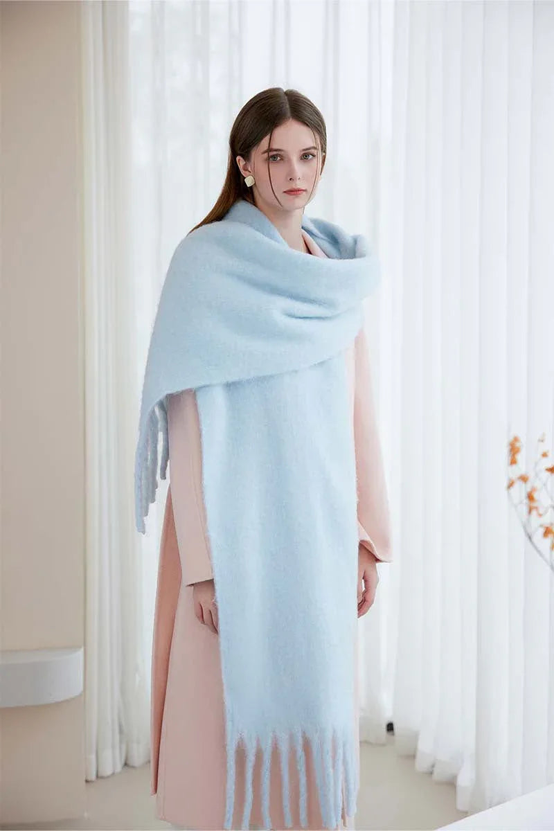 Full body shot of a woman wearing a light blue oversized scarf with fringe detail over a pink coat.