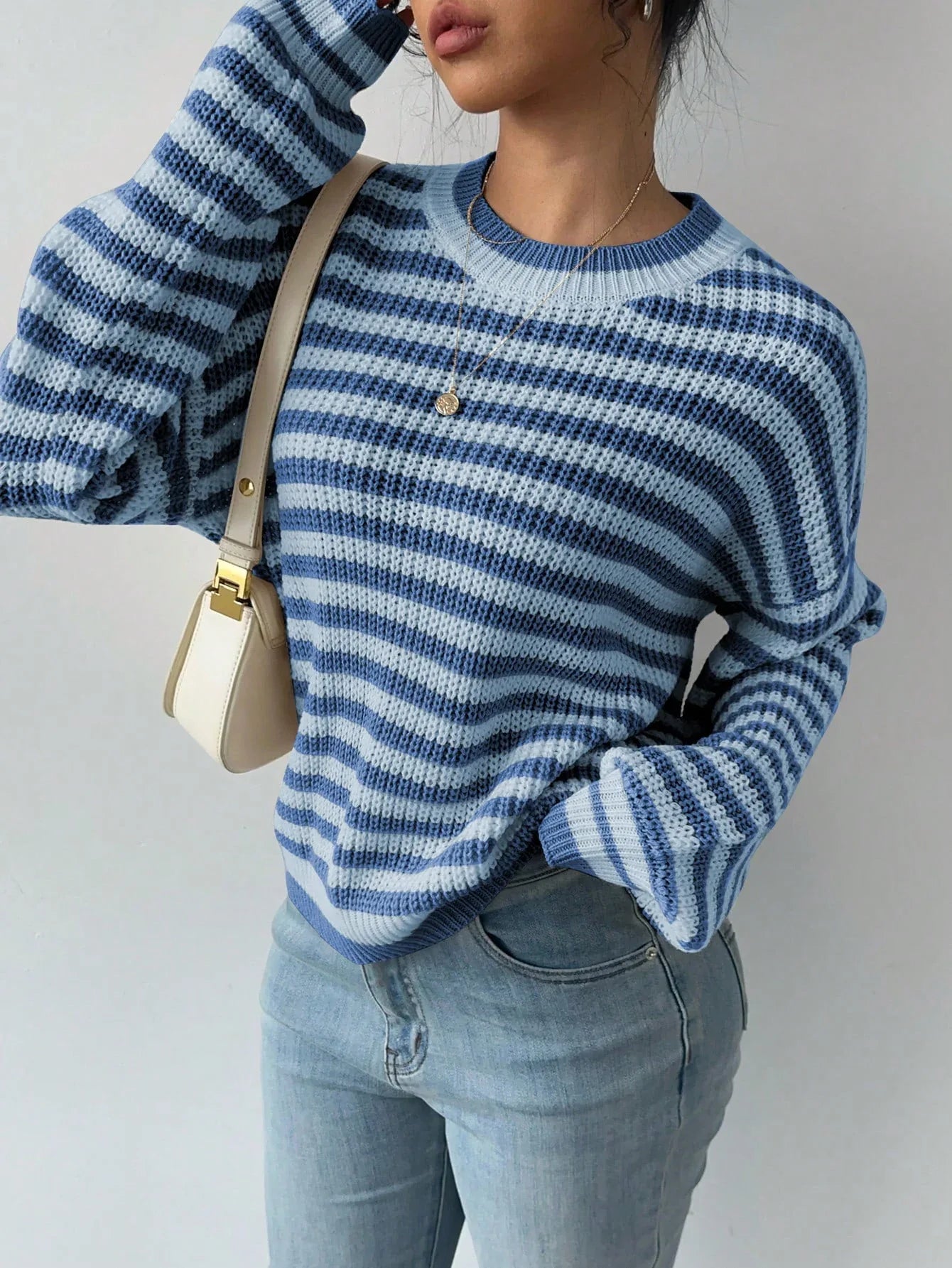 Close-up of a woman wearing a blue and white striped knit sweater with light wash denim jeans