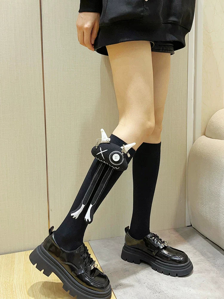 Black knee-high socks with a black fabric applique featuring white horns and dangling legs with white accents