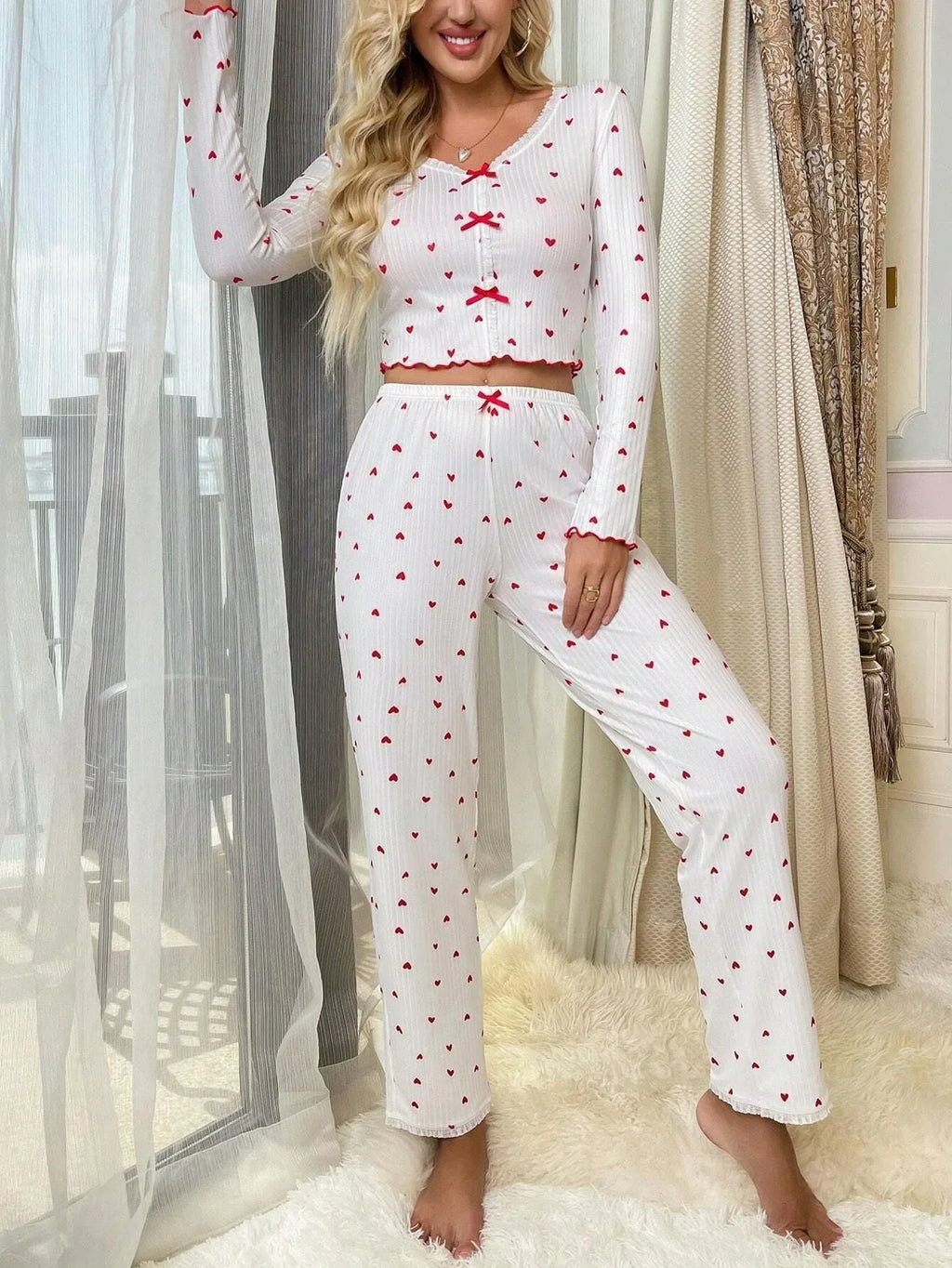 Woman wearing white pajamas with red hearts and red scalloped trim, standing in a room with red heart balloons.