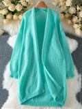 Teal longline chunky knit cardigan laid flat on a fluffy white rug with floral decorations.