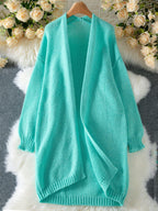 Teal longline chunky knit cardigan laid flat on a fluffy white rug with floral decorations.