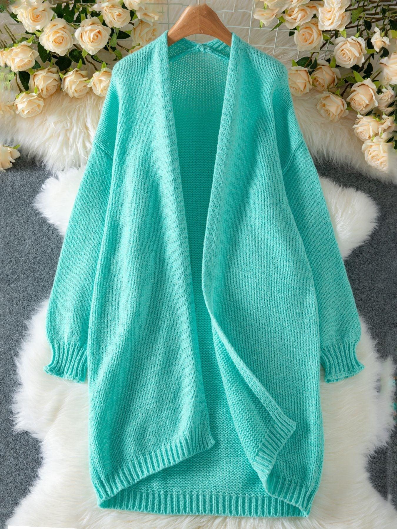 Teal longline chunky knit cardigan laid flat on a fluffy white rug with floral decorations.