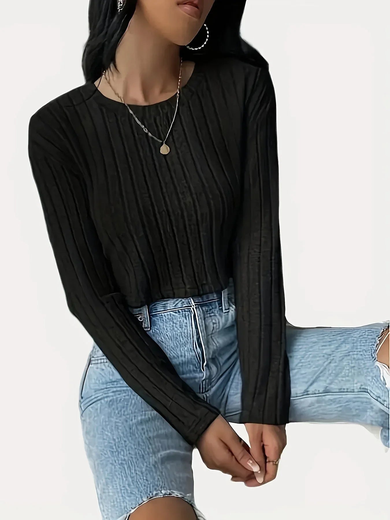 Woman wearing a black ribbed cropped long-sleeve shirt and light wash jeans, seated, side view